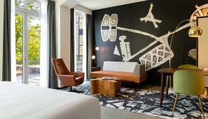 A hotel room with a bed, a sofa, a coffee table, and a dining area with a chair and table.