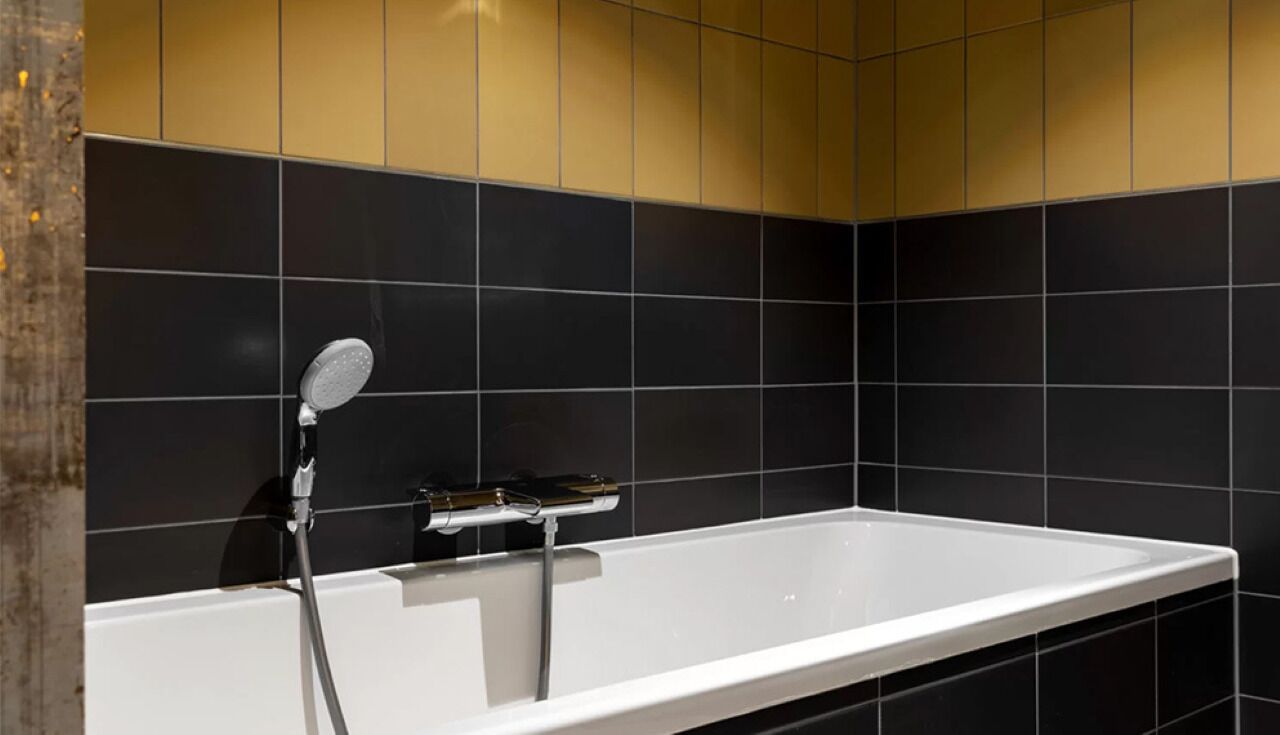 Een moderne badkamer met een witte badkuip, zwart-gouden tegels en een handdouche.