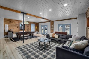 A spacious living area with a pool table, sofa, and a checkered rug.