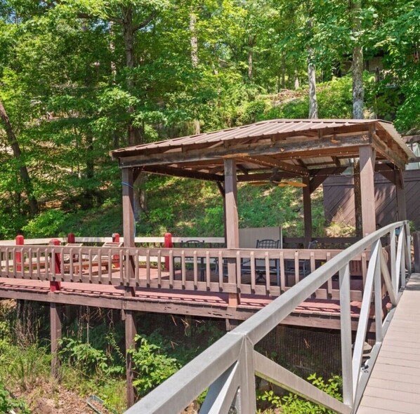 A wooden deck with a pergola, surrounded by greenery.