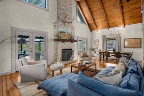 A spacious living room with a stone fireplace, a dining area, and a large window overlooking the outdoors. - Best Lakeside Living at Big Bend Retreat! (Houston)