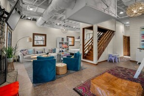 A spacious living area with a sofa, blue armchairs, a coffee table, a patterned rug, and a staircase.