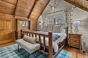A cozy bedroom with a wooden bed, a bench, a bedside table, and a window with curtains.