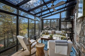 A sunroom with large windows, a ceiling fan, a sofa set, and a small table.