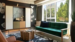 Un salón moderno con un sofá verde, una mesa de centro de madera y un ventanal con vistas a árboles.