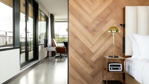 Una habitación de hotel moderna con un ventanal grande, una pared de madera en patrón espiga, una mesita de noche con lámpara y una cama.