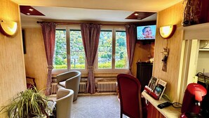 Una habitación acogedora con un ventanal grande, un radiador, una silla roja, un televisor y una cafetera.
