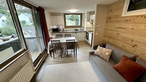 A compact kitchen with a dining area, a sofa with cushions, and a window with curtains. - Le Capucin 79 - Le Mont Dore (Mont-Dore)