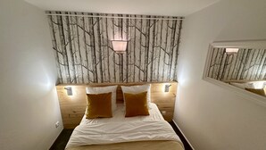 A bedroom with a bed, two bedside lamps, a mirror, and a wall with a tree pattern. - Le Capucin 79 - Le Mont Dore (Mont-Dore)