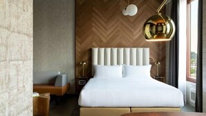 Een moderne hotelkamer met een groot bed, een houten hoofdbord, een nachtkastje en een lamp.