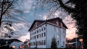 Ein großes, mehrstöckiges Gebäude mit einer symmetrischen Fassade, einem zentralen Eingang und einem umlaufenden Kopfsteinpflasterhof.