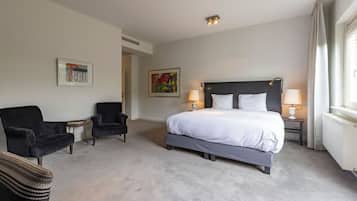 Habitación de hotel con una cama grande, dos sillones, una mesita y dos lámparas de pared.