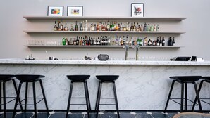 A bar area with three black stools, a marble countertop, and shelves stocked with various liquor bottles and glasses. - Comfortable Stay! Free Parking, Onsite Dining! Close to Stuw Belfeld! (Baarlo)