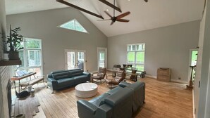 Un ampio soggiorno con soffitto alto, pavimento in legno e grandi finestre che lasciano entrare la luce naturale. Sono presenti diverse zone relax, tra cui un divano e un tavolino rotondo.