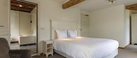 A bedroom with a large bed, a nightstand, a chair, and a bathroom with a shower and bathtub.