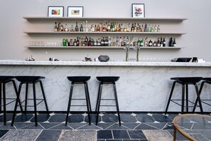 Zona de bar con encimera de mármol, varios taburetes y estantes llenos de botellas y copas.