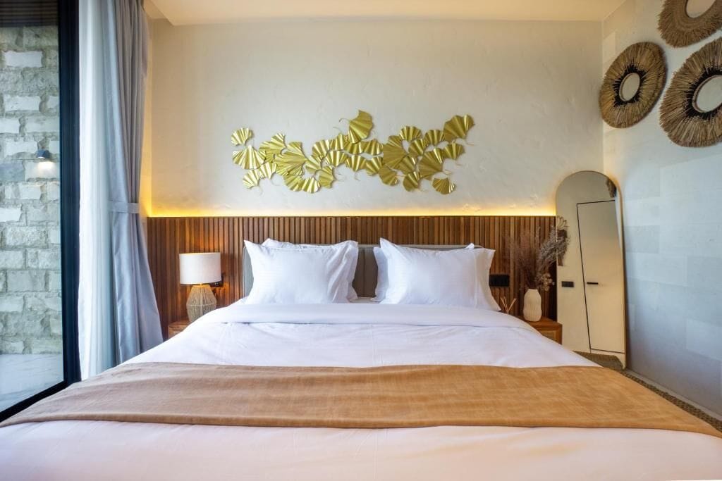 Une chambre d’hôtel comprenant un lit, un élément décoratif représentant une feuille fixé au mur, une lampe de chevet et un miroir.