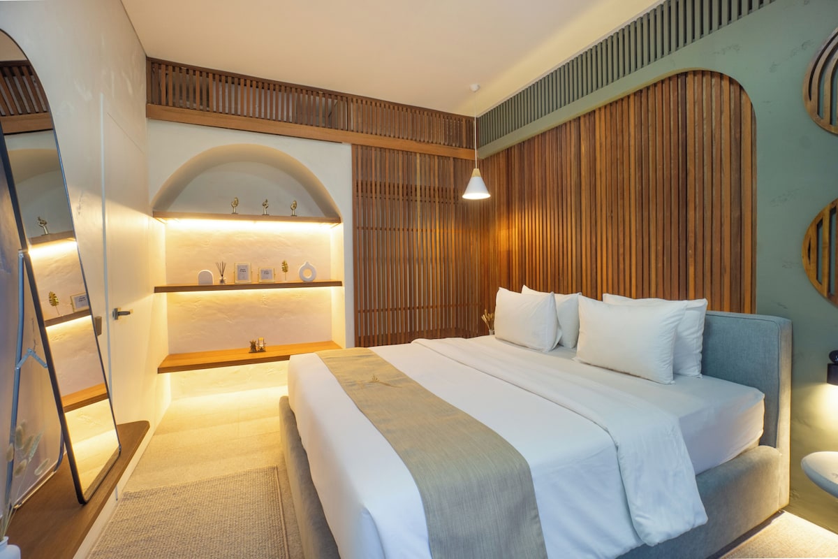 A modern bedroom with a large bed, wooden paneling on the walls, and a built-in shelf with decorative items.