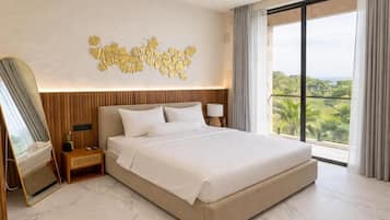 A hotel room with a large bed, a bedside table, a nightstand, a wall-mounted mirror, and a view of greenery through the window.