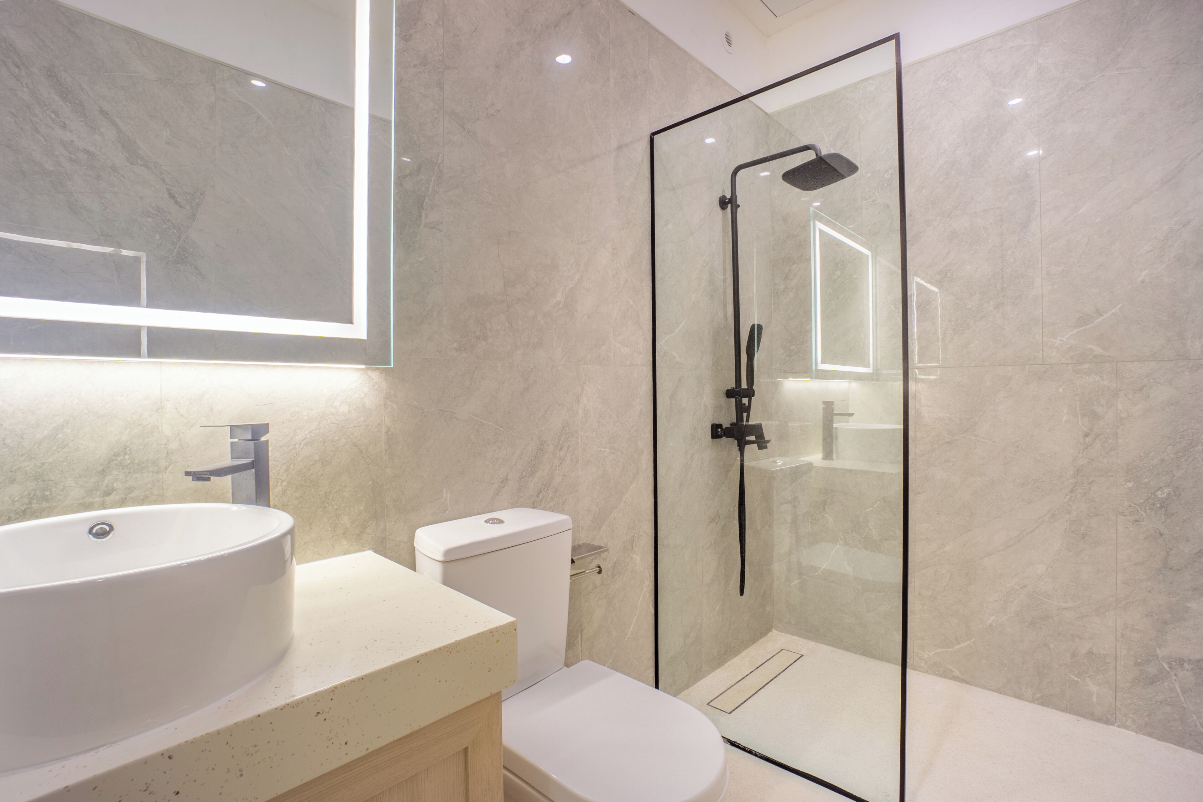 Un baño moderno con ducha envuelta en vidrio, un lavamanos blanco y un inodoro.
