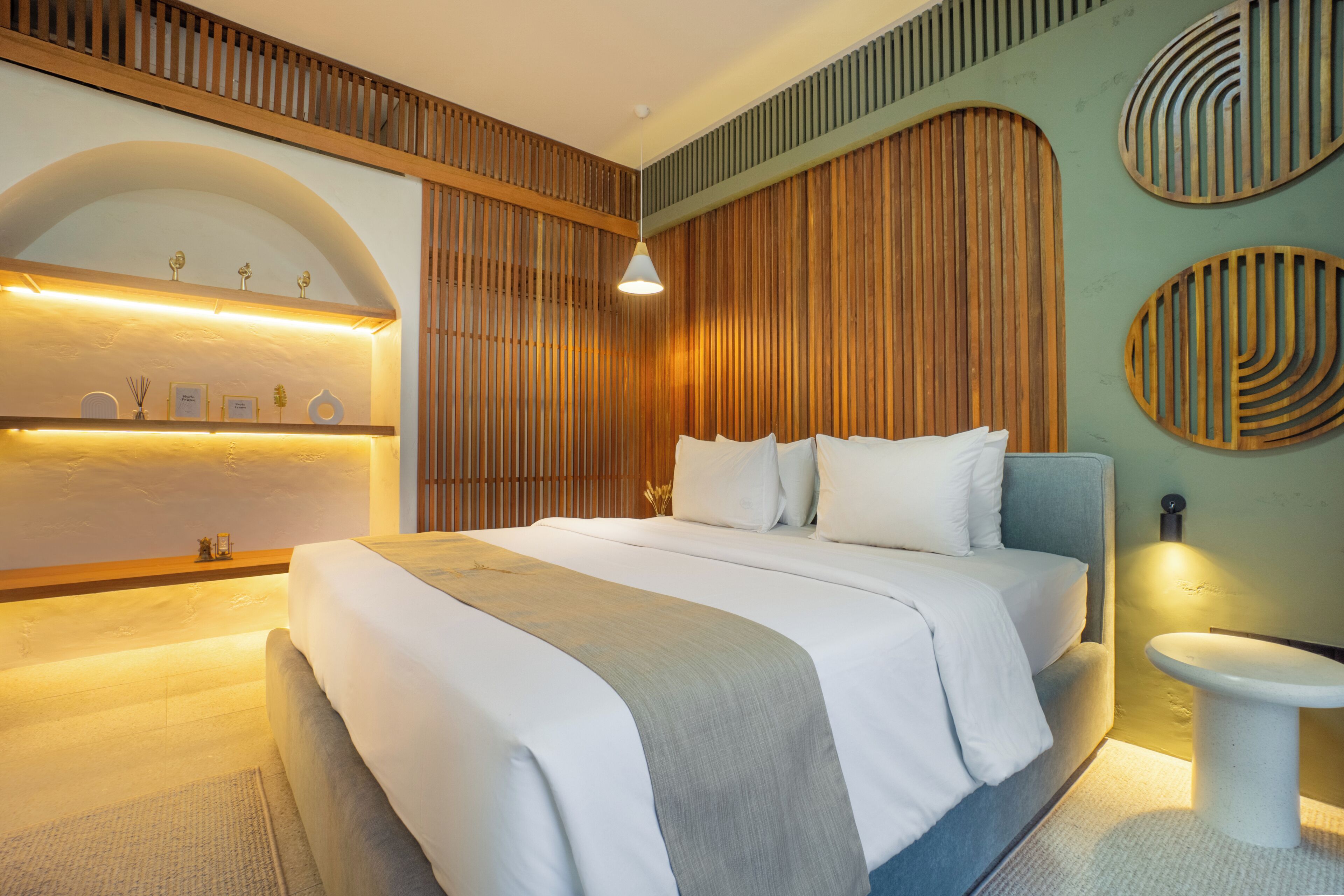 Une chambre moderne avec un grand lit, une table de chevet, une étagère murale agrémentée d’objets décoratifs et un panneau mural en bois au design original.