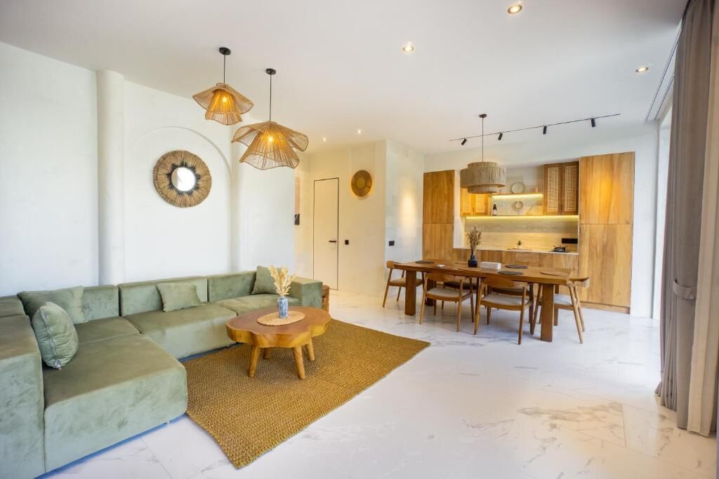 A modern living room with a green sofa, a wooden coffee table, and a dining area with a wooden table and chairs.