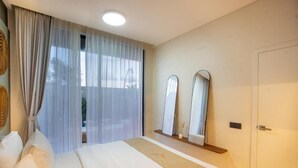 A hotel room with a bed, a large window with sheer curtains, a bedside table, and two wall-mounted mirrors. - White Residence (KUTA SELATAN)