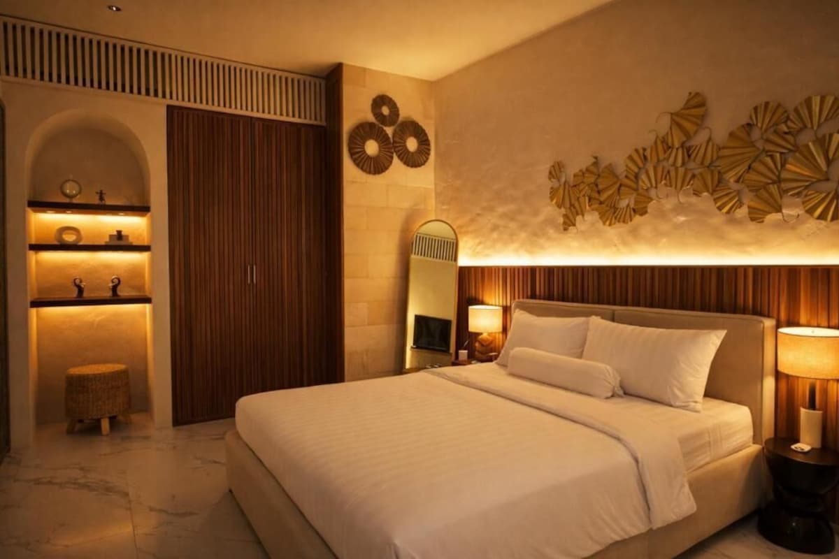A hotel room with a large bed, a wooden wardrobe, a vanity with a mirror, and wall-mounted decor.