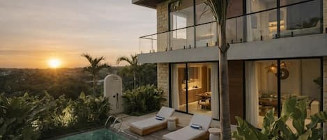 A modern two-story house with a pool, lounge chairs, and a view of the sunset.
