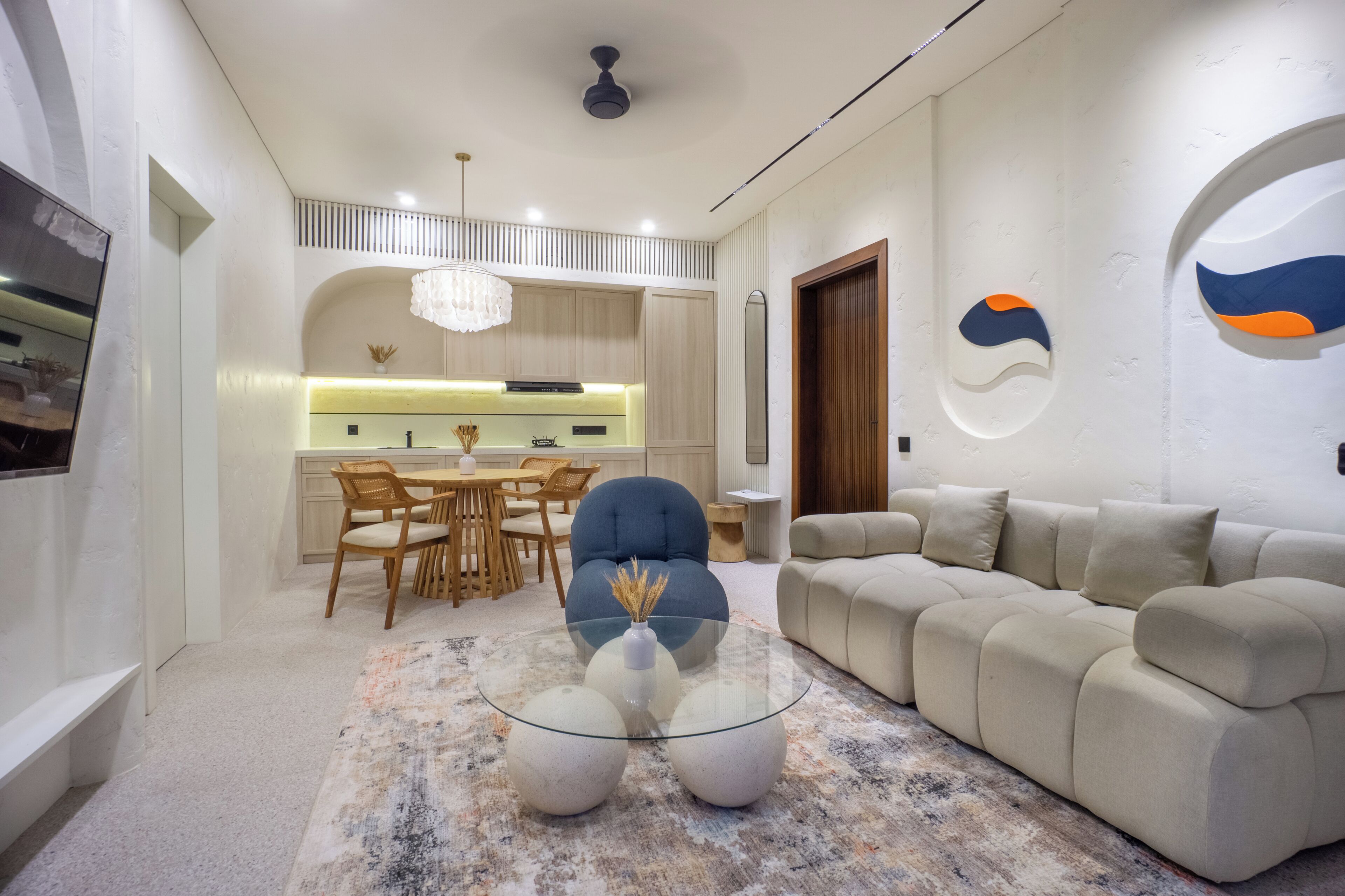A modern living room with a glass coffee table, a beige sofa, and a dining area with wooden chairs.