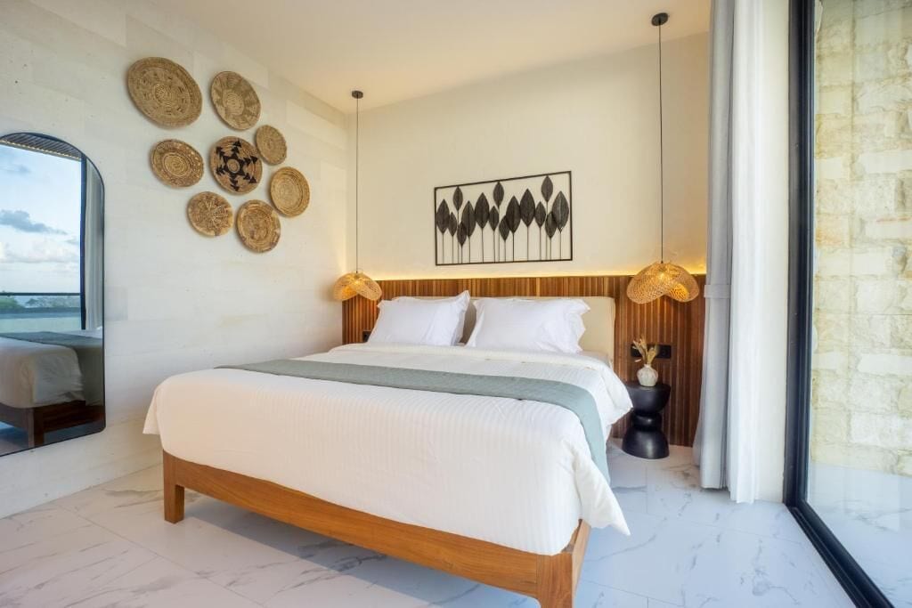 A modern bedroom with a wooden bed, white bedding, a wall-mounted artwork, and a large window.
