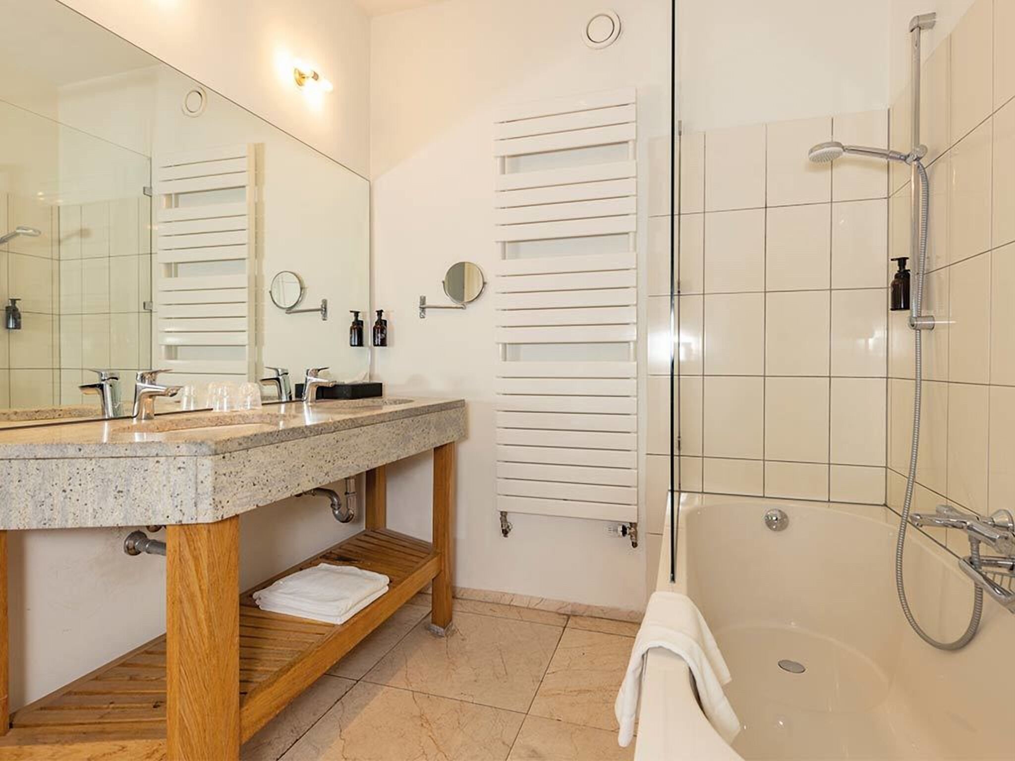 Un baño moderno con lavamanos de granito, tocador de madera, un espejo grande, cerramiento de ducha de vidrio y una bañera.