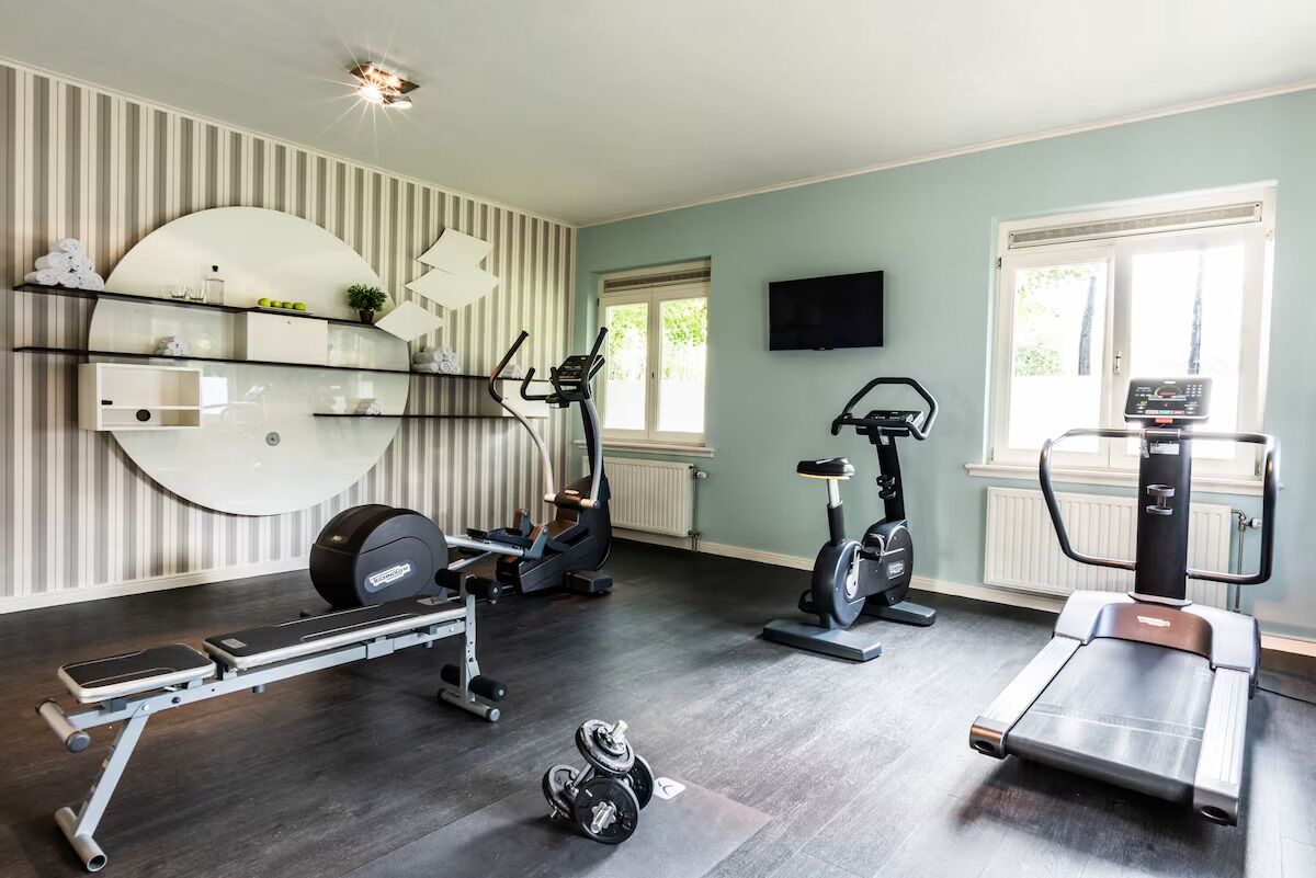 Ein Heimfitnessraum mit Laufband, Crosstrainer, Ergometer und Gewichtbank.