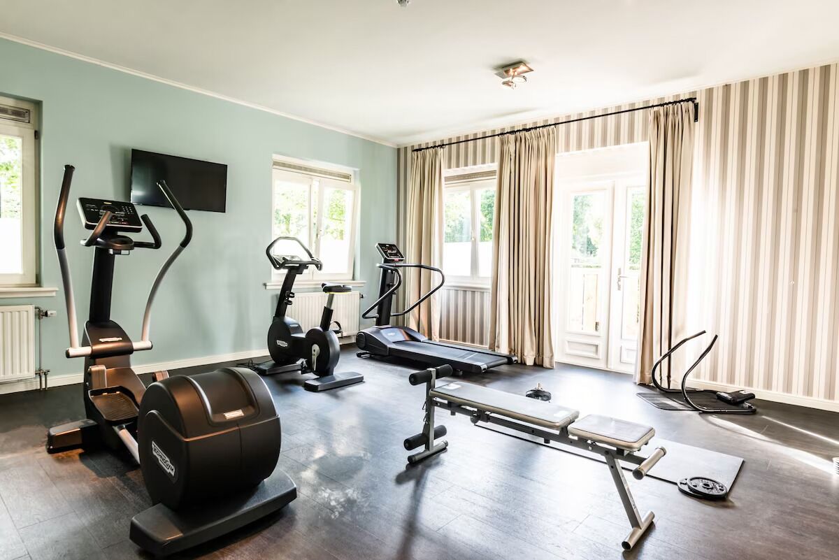 Un gimnasio en casa con equipo de ejercicio, ventanas amplias y vista a zonas verdes.