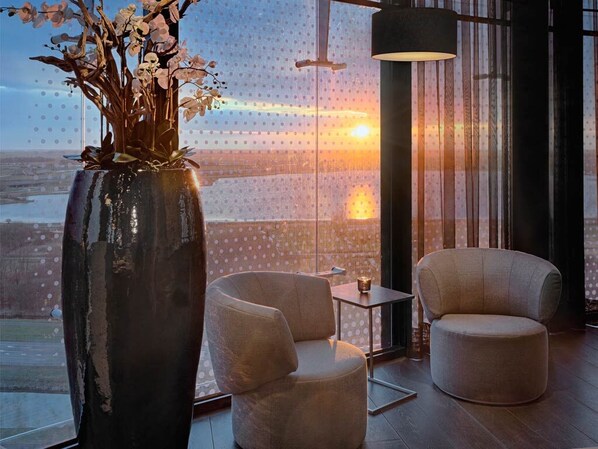 Une chambre moderne avec une grande fenêtre, deux fauteuils, une petite table et un vase rempli de fleurs.