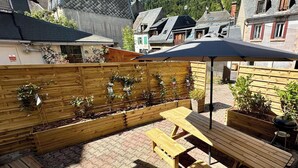 A patio area with wooden benches and a table, surrounded by a wooden fence with plants. - Retreat With Terrace, Parking (Mont-Dore)
