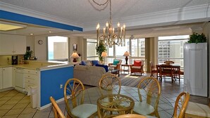 Un vaste espace de vie avec un coin salon central, une cuisine dotée de meubles blancs et un balcon offrant une vue agréable.