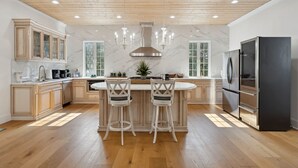 A modern kitchen with wooden cabinets, a central island, bar stools, a black refrigerator, and a chandelier. - Blue Southern Charm 7 Bedroom Home (Georgetown)