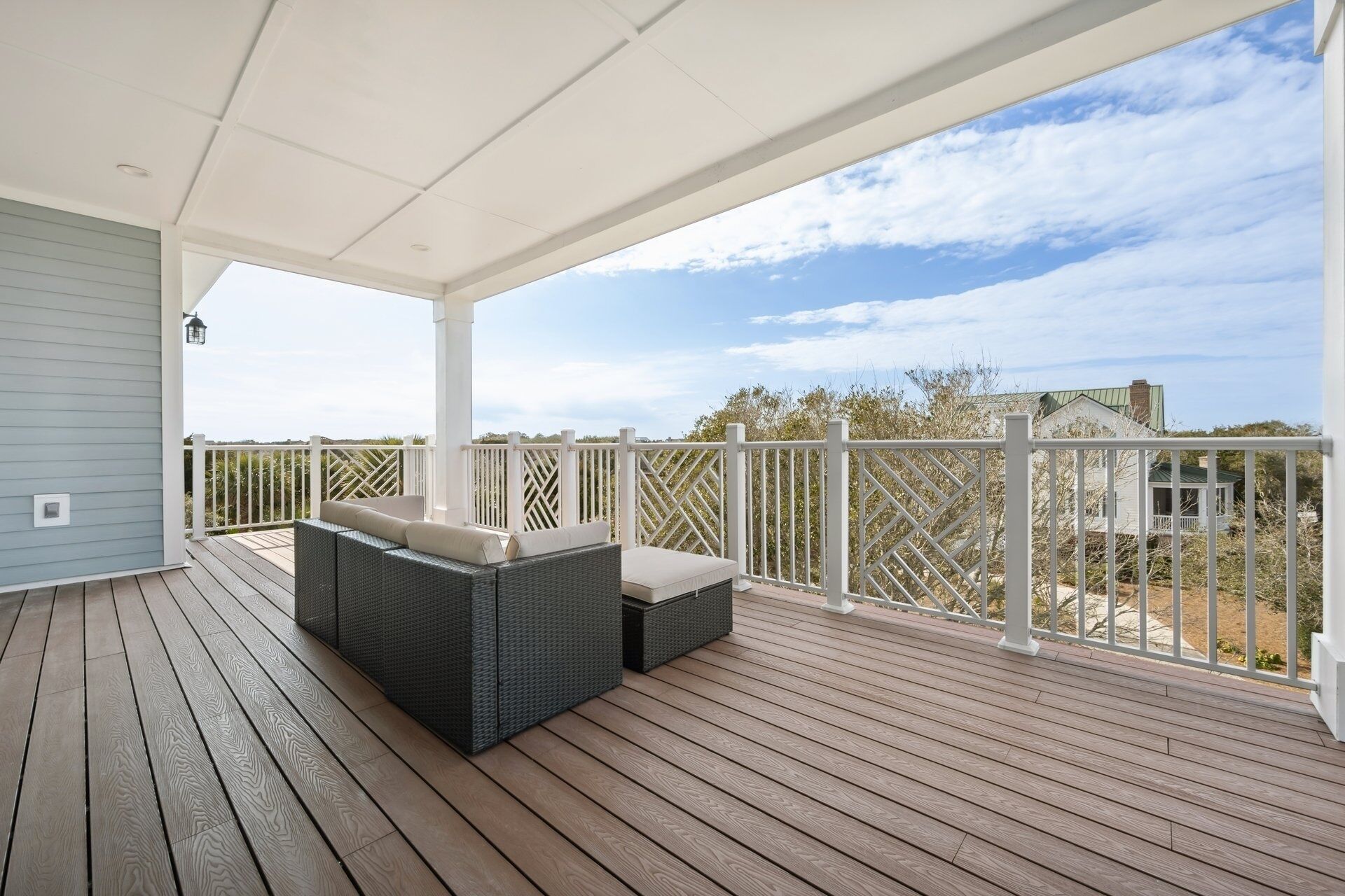 A covered outdoor deck with wicker furniture, a white railing, and a view of the surrounding landscape.