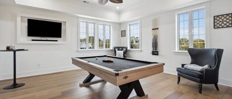 A spacious room with a pool table, a comfortable armchair, and a television mounted on the wall.