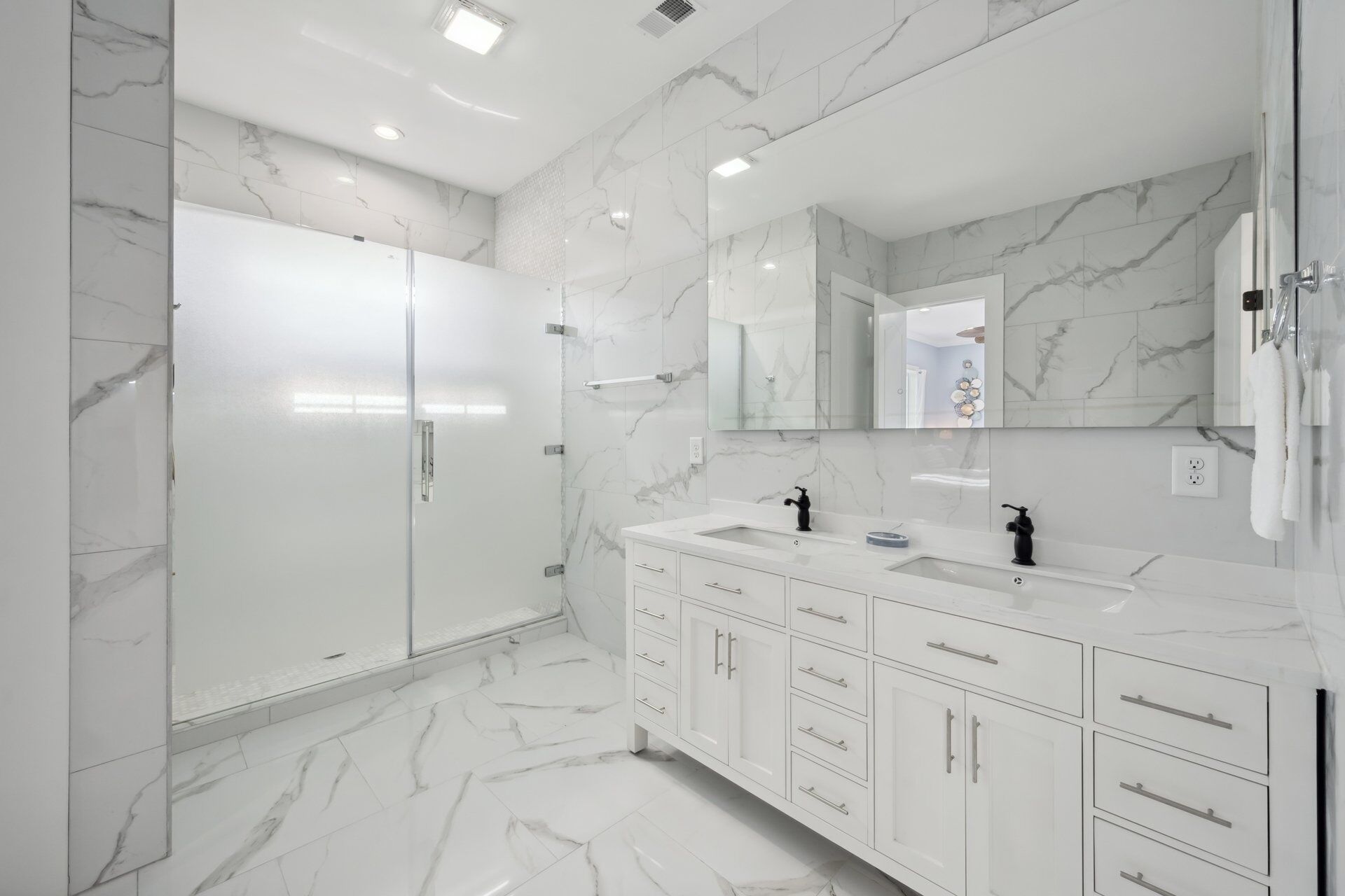 A modern bathroom with marble walls and floors, a large mirror, and a white vanity with multiple drawers and a sink.