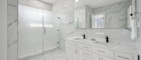 A modern bathroom with marble walls and floors, a large mirror, and a white vanity with multiple drawers and a sink.