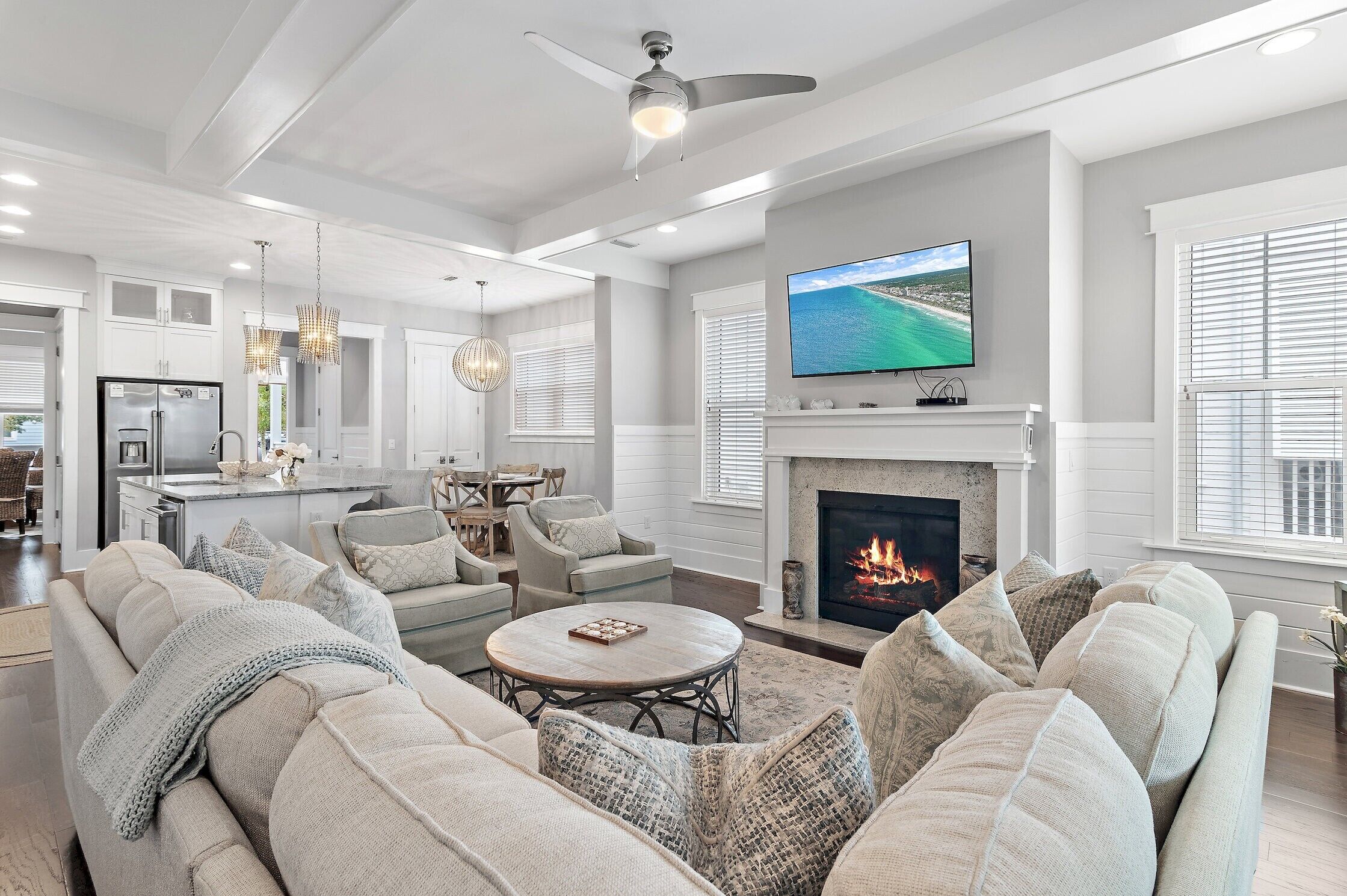 A spacious living room with a fireplace, a television, and a dining area with a kitchen in the background.