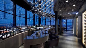 Een moderne bar met een panoramisch uitzicht over de stad, een uniek plafondontwerp en een selectie wijnflessen.