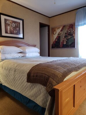 Una camera da letto con un letto a struttura in legno, una coperta trapuntata e due cuscini. Sulla parete c'è un quadro incorniciato e un dipinto che raffigura una scena rustica.
