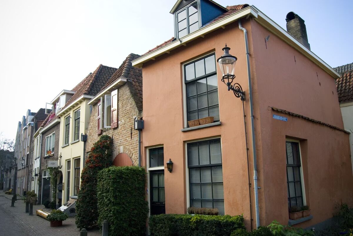 Een rij traditionele Europese gebouwen met gelijke gevels, grote ramen en een straat vol groen.