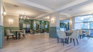 Un salon spacieux et bien éclairé, doté d’un parquet, de murs verts et de plusieurs coins salon.