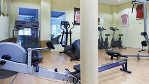 Un gimnasio con máquinas de cardio, bancos para pesas y un espejo grande.