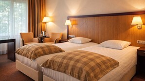 Una habitación de hotel con dos camas, un escritorio, una silla y dos lámparas fijadas a la pared.