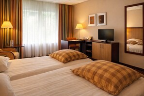 Een hotelkamer met twee bedden, een bureau, een stoel, een televisie en een spiegel.